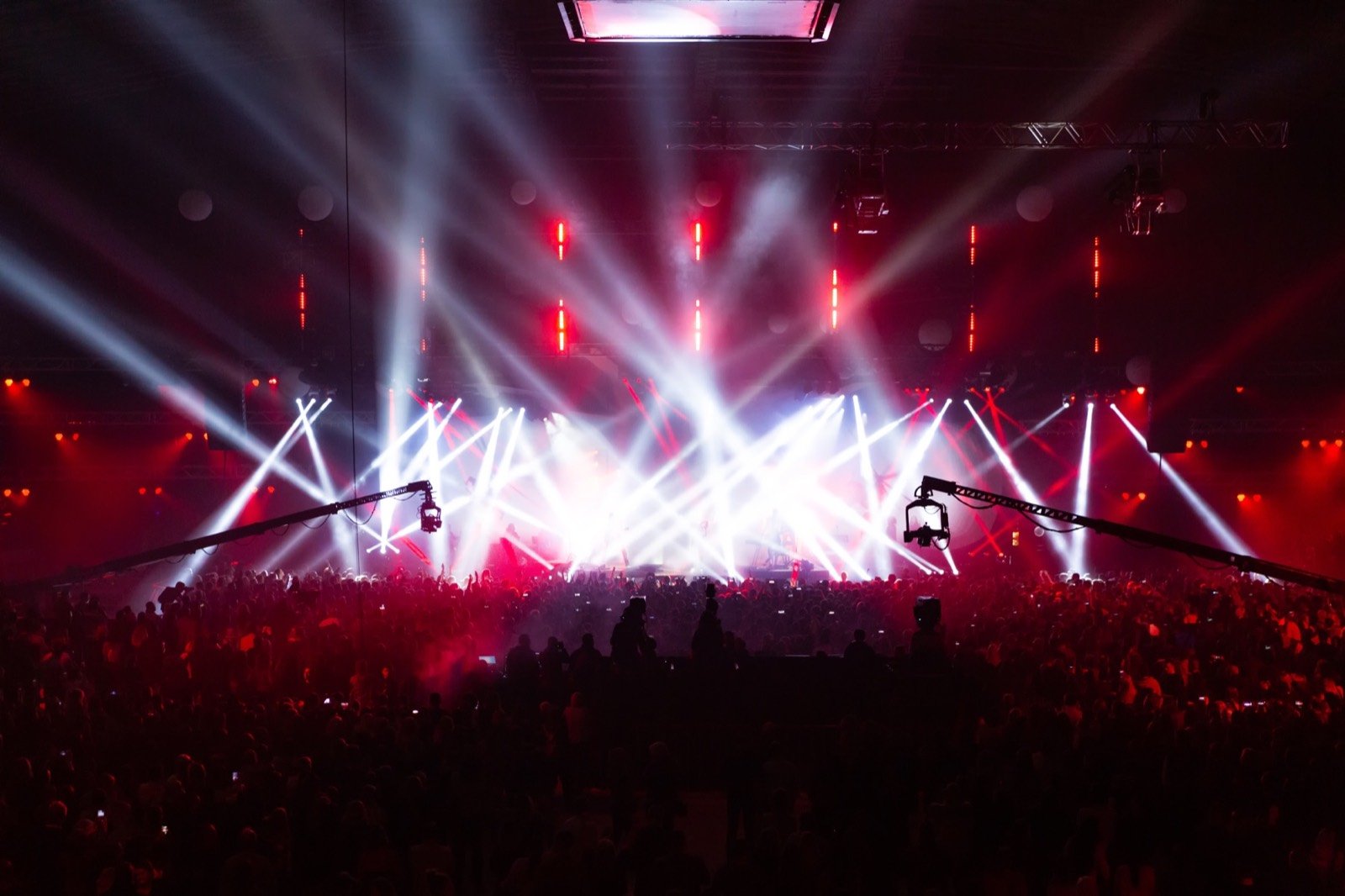 Large indoor production framed by bright stage beams and broadcast cameras
